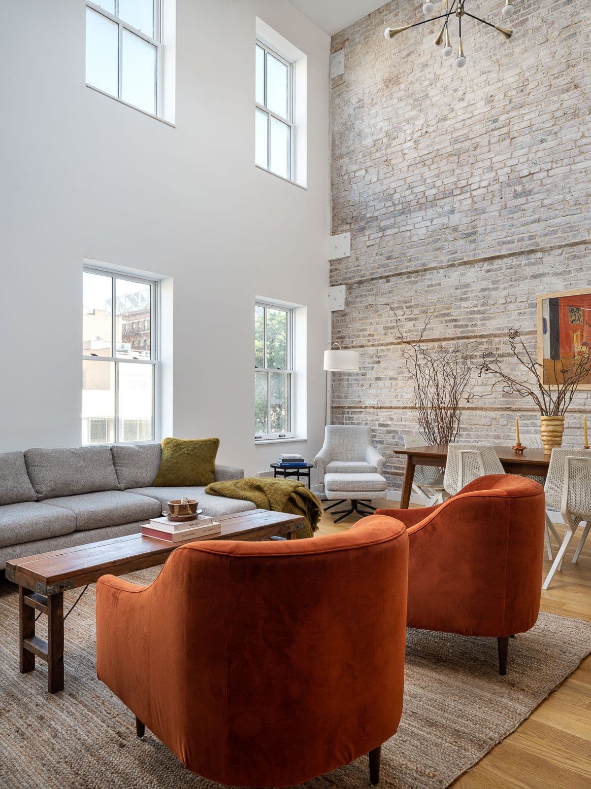 Double height ceiling living room with 2 orage accent chairs, sofa, bench